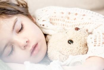 young girl in bed sleeping holding a teddy bear